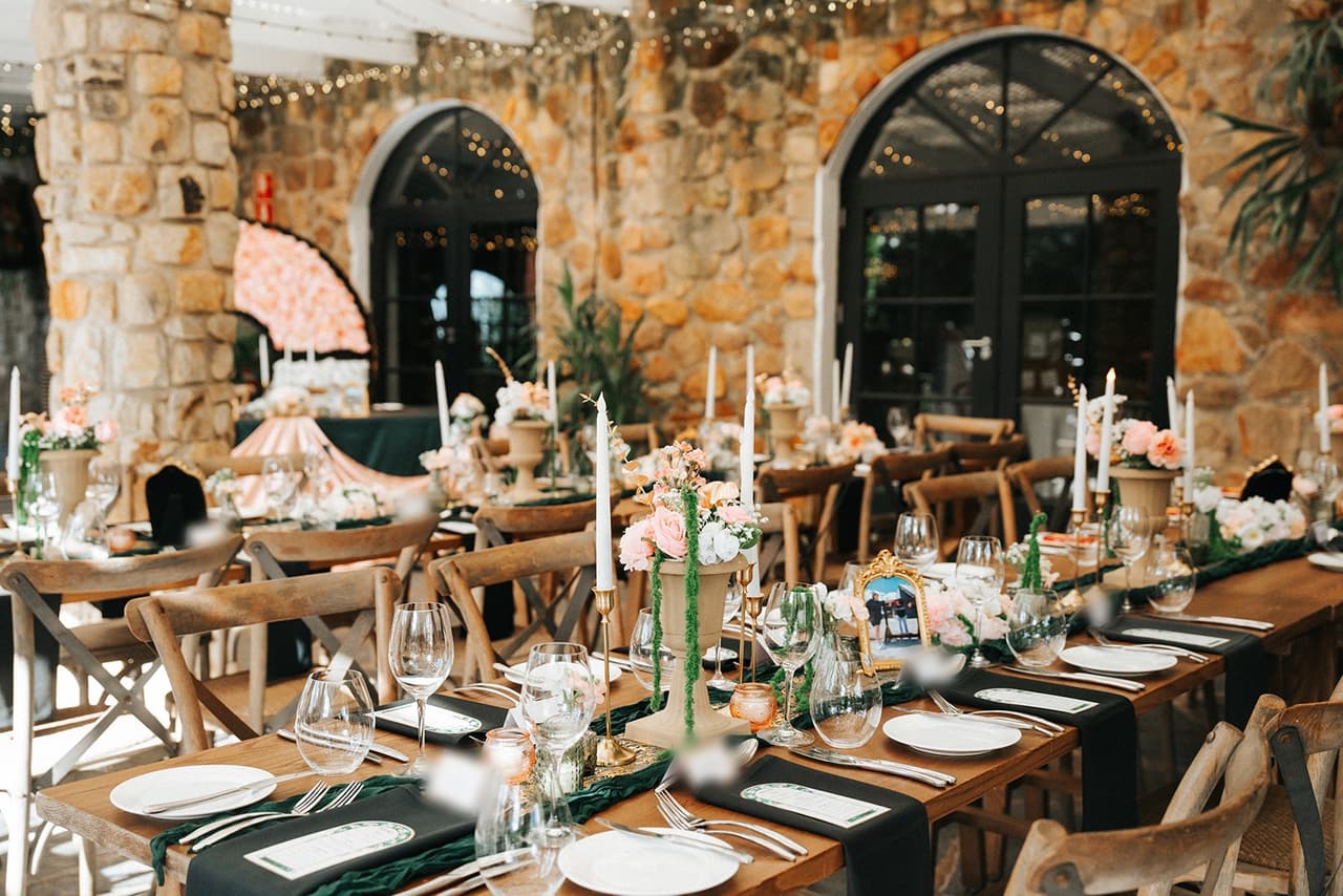 Long reception tables with candles, pink roses and green runners in front of the arched stone windows