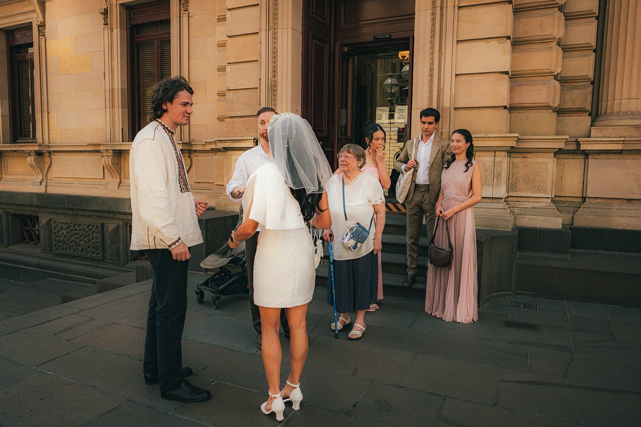 Cecile, Stefan and their guests on the footpath outside the registry entrance after the ceremony, the sandstone facade and timber doors behind them