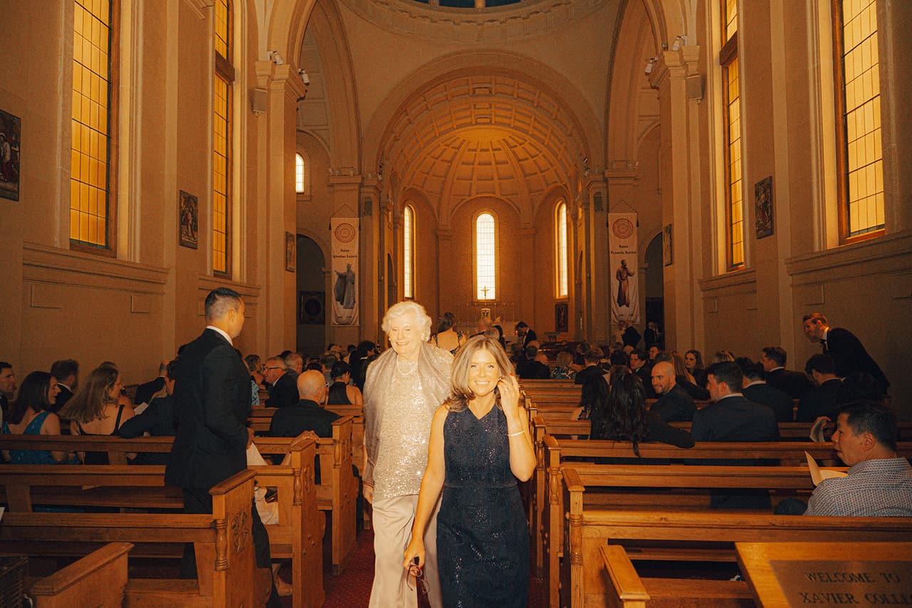 Guests arriving along the nave of the chapel, the altar and its tall arched windows at the far end
