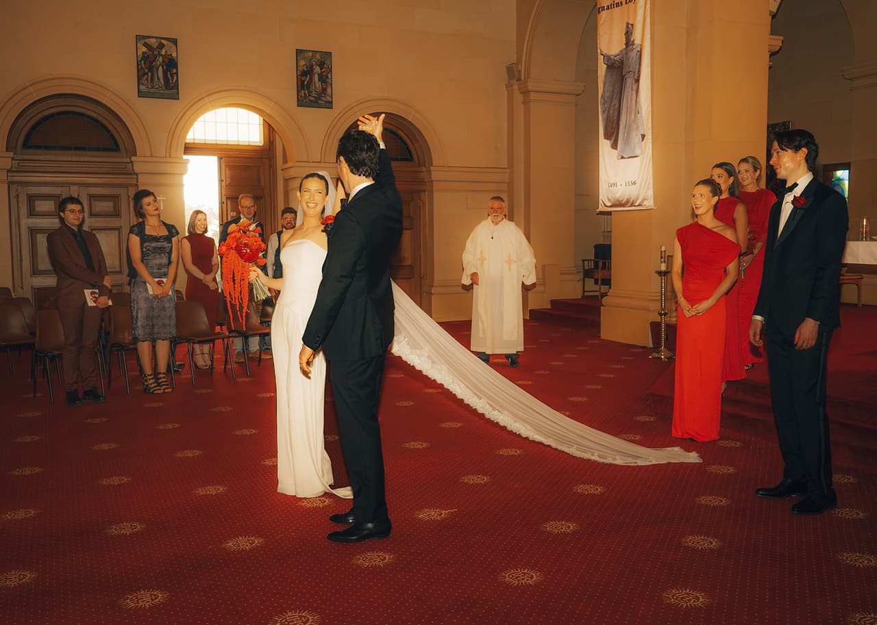 Kira and Nick turning to walk back down the aisle, her long veil spread over the red carpet