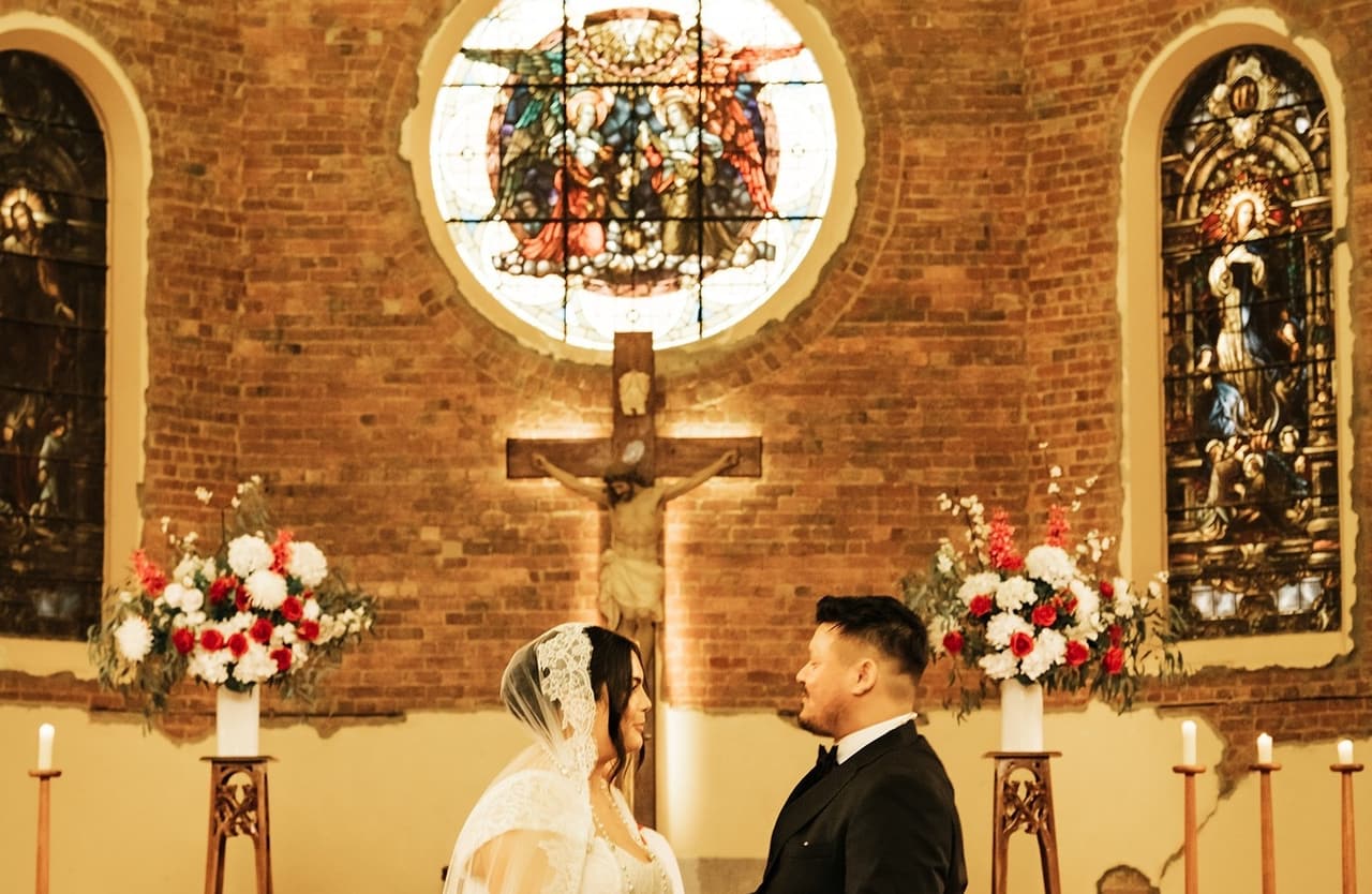 Ashley and Bryan facing each other at the altar under the crucifix and stained glass