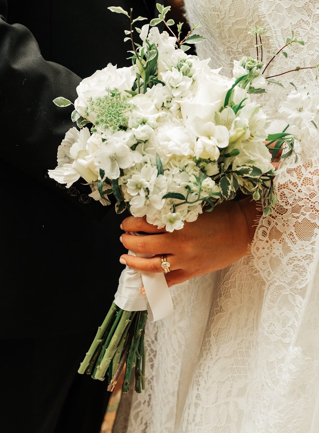 Close up of Ashley’s white bouquet and her rings against the lace of her gown