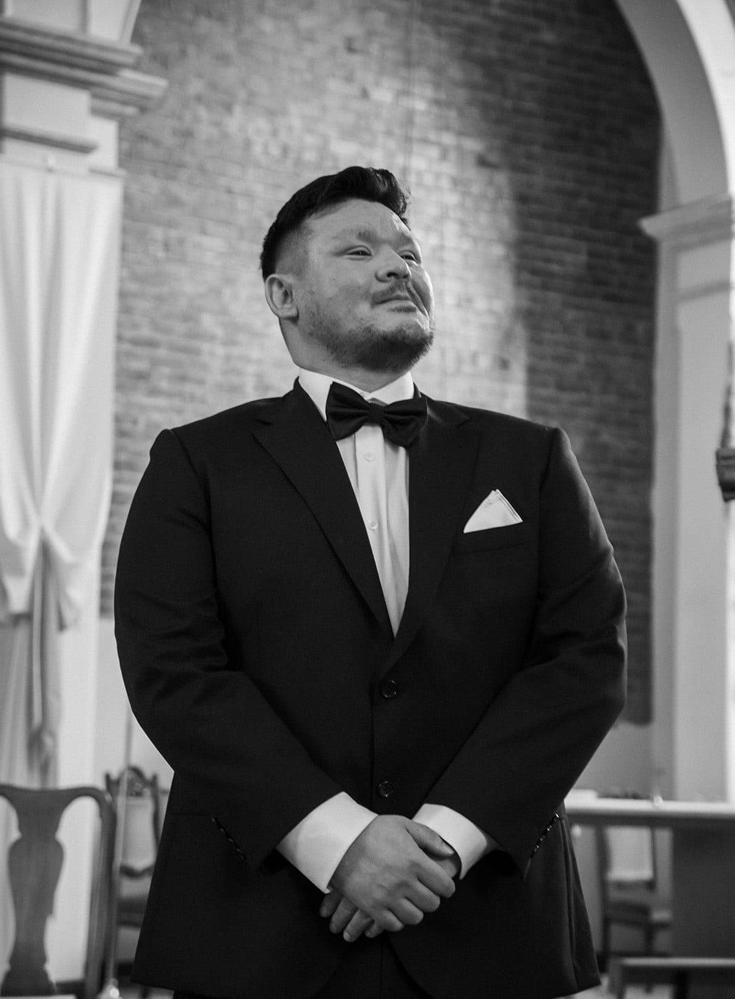 Black and white photo of Bryan waiting at the front of the church, hands clasped