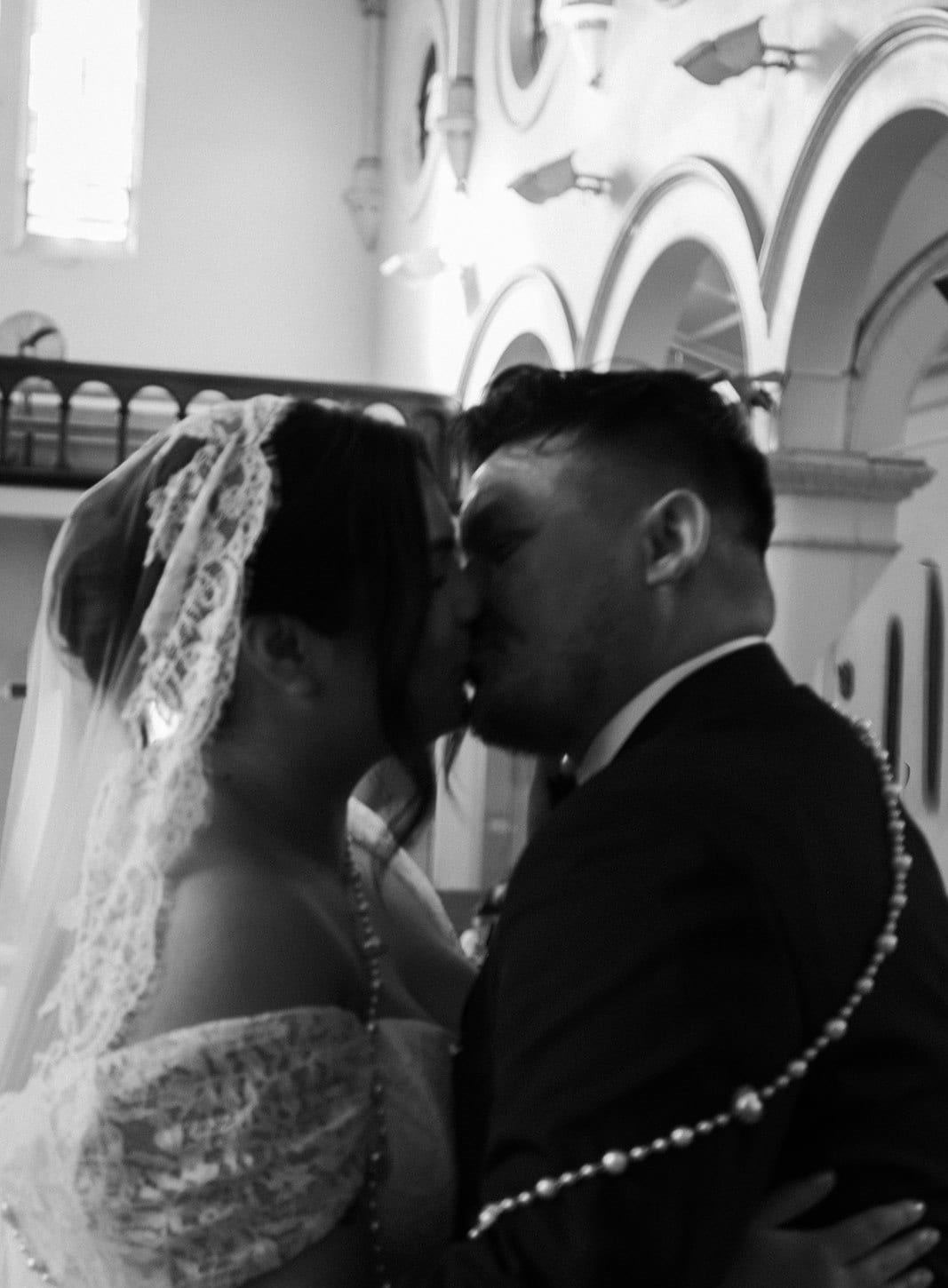 Black and white photo of Ashley and Bryan kissing with the rosary cord around their shoulders