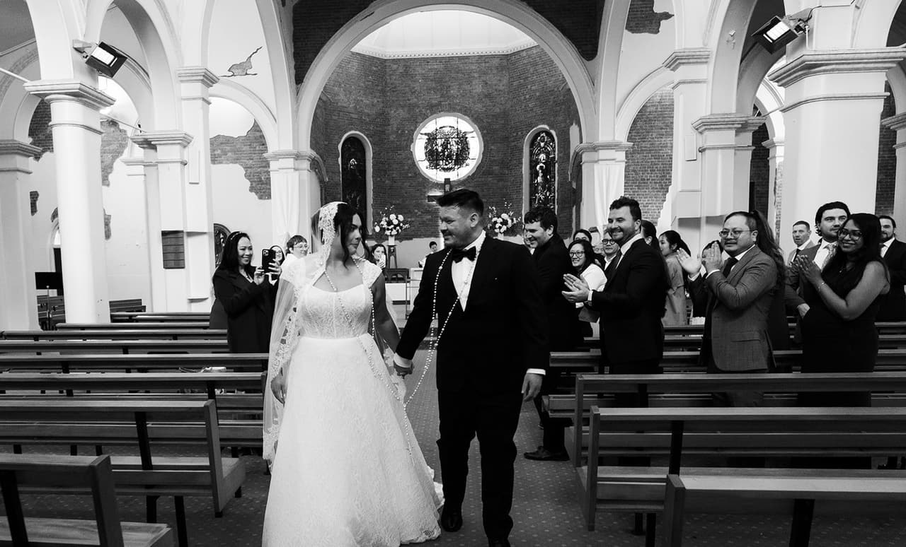 Black and white photo of Ashley and Bryan walking back up the aisle as their guests clap