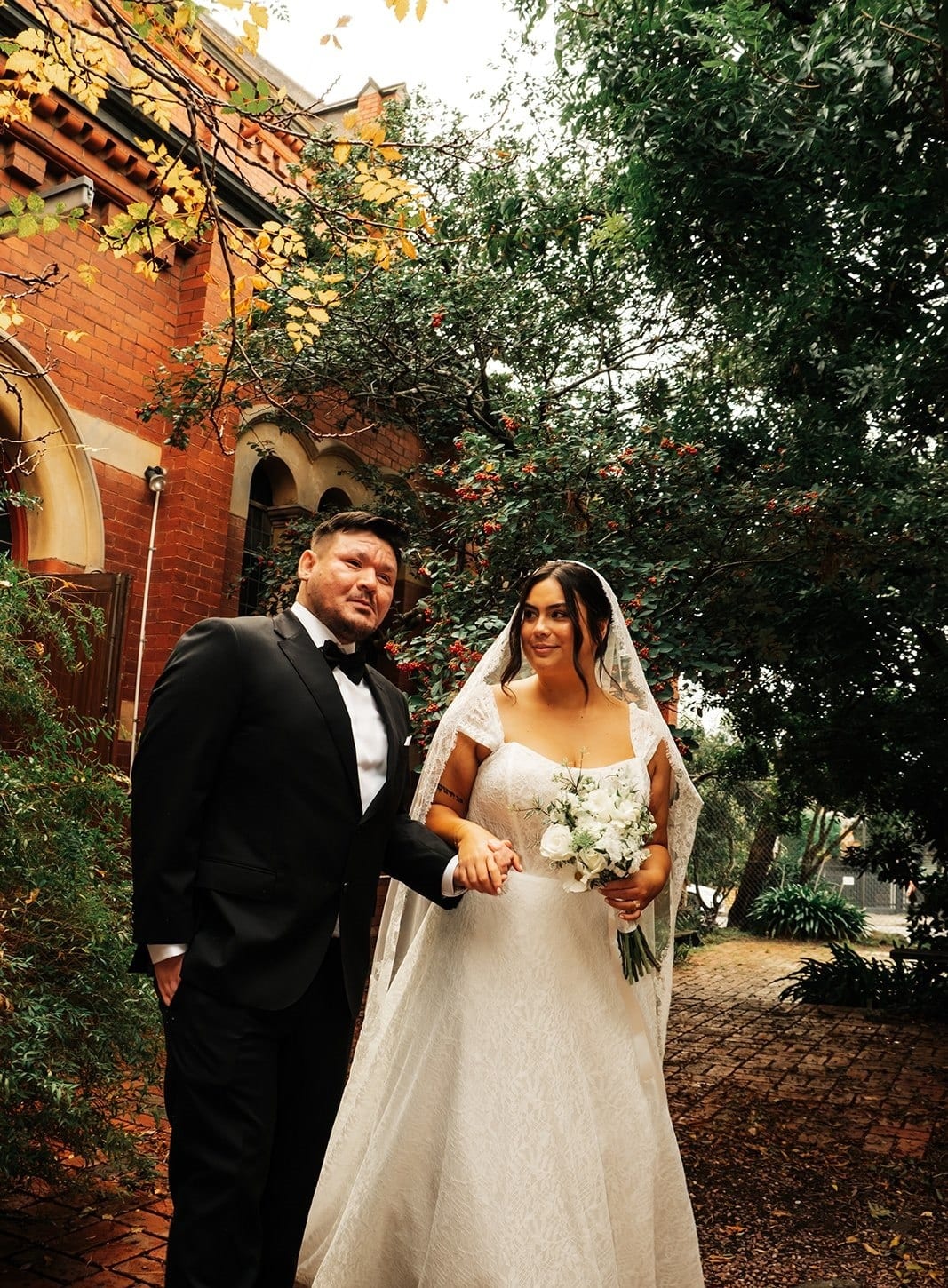 Ashley and Bryan walking arm in arm along a brick path in the church garden