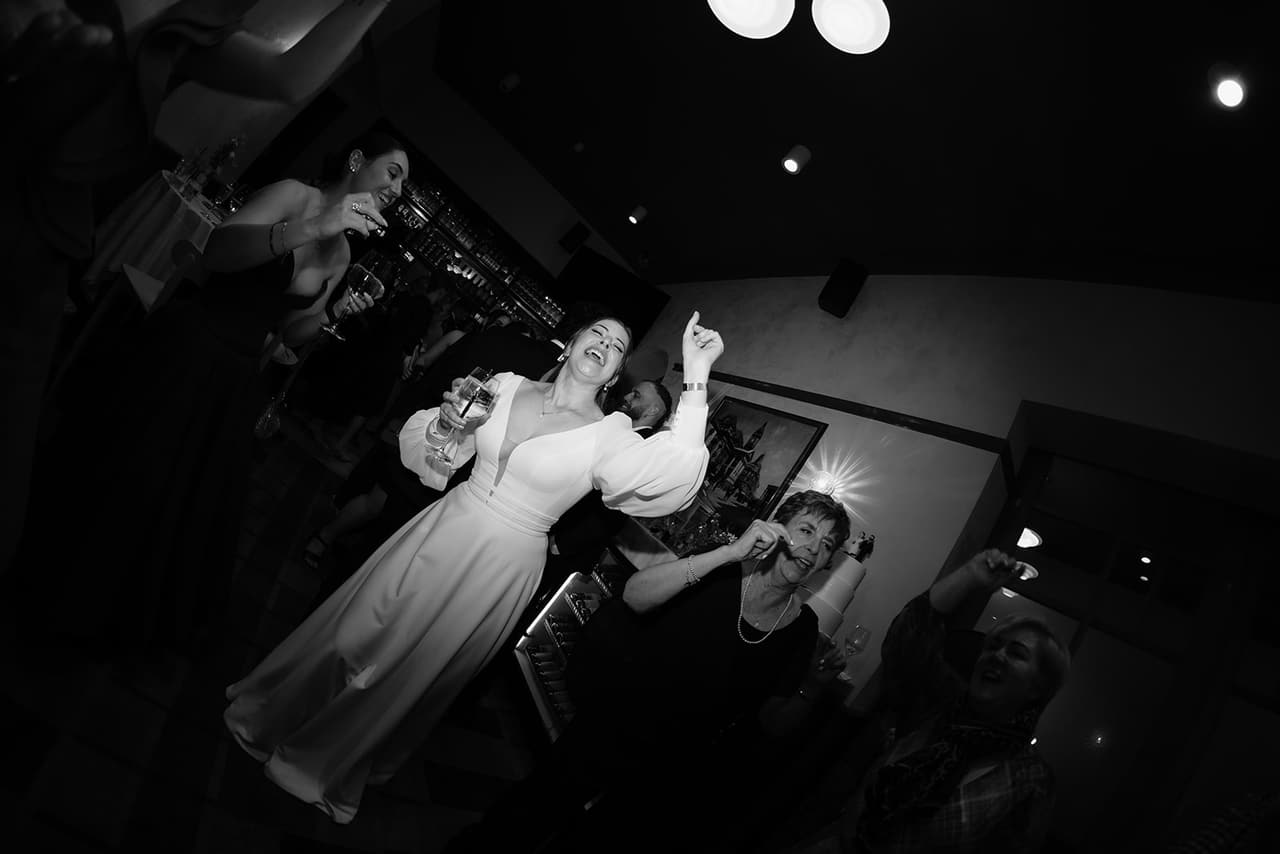 Black and white photo of Bianca dancing with her arms in the air among her guests