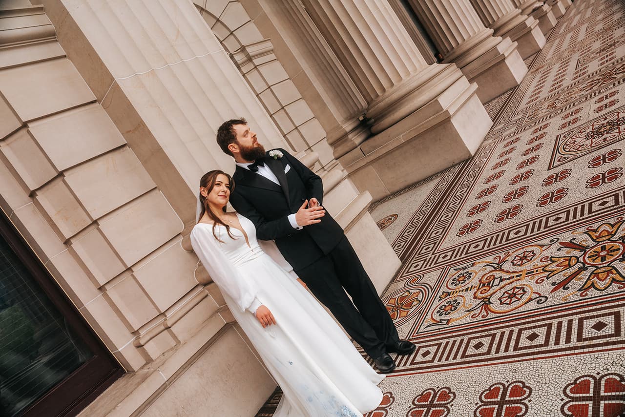 Bianca and Aidan in the colonnade of Parliament House, patterned tiles at their feet
