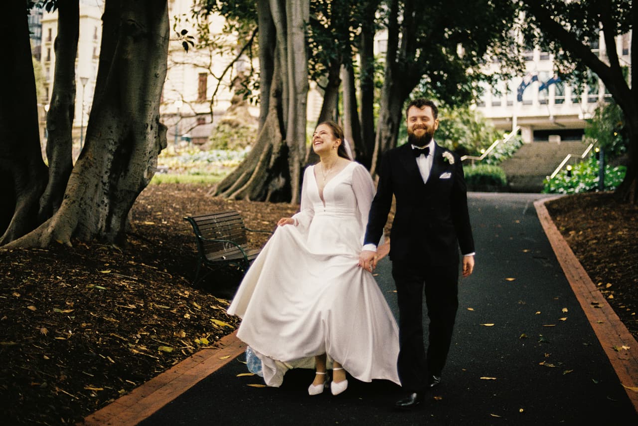 Bianca and Aidan walking hand in hand along an avenue of old trees, on 35mm film