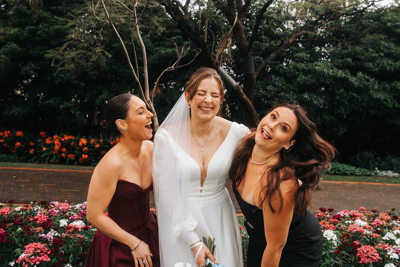 Bianca laughing with two friends in front of beds of pink and red flowers