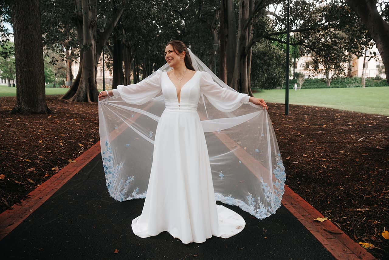 Bianca holding her veil out wide in an avenue of old trees
