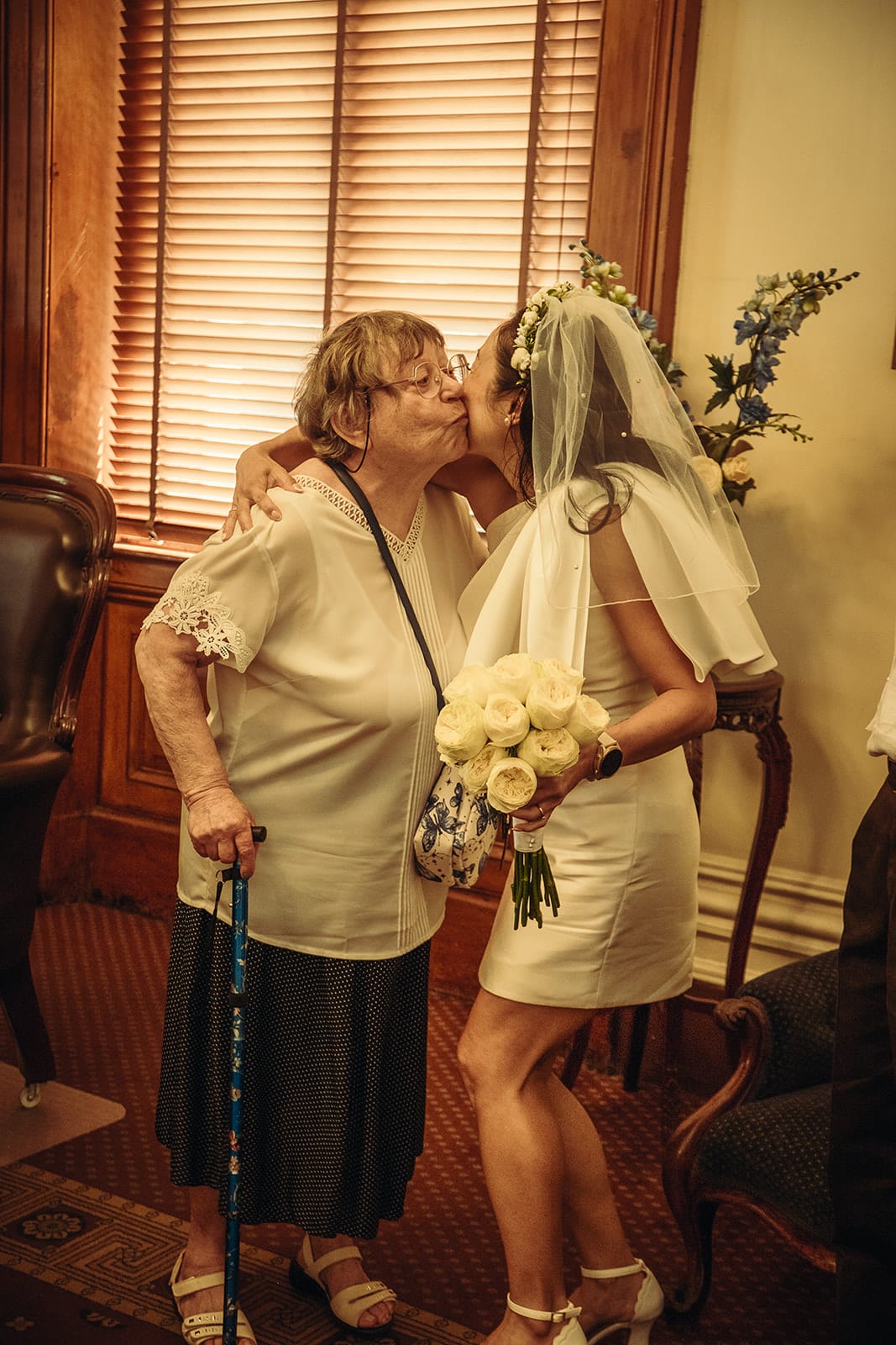 An older guest with a walking stick kissing Cecile on the cheek by the tall window