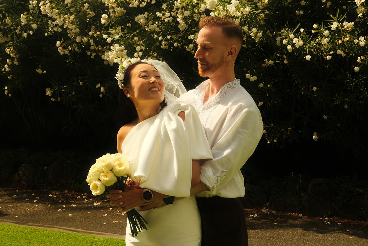 Cecile laughing in Stefan's arms among flowering bushes, yellow roses in her hands