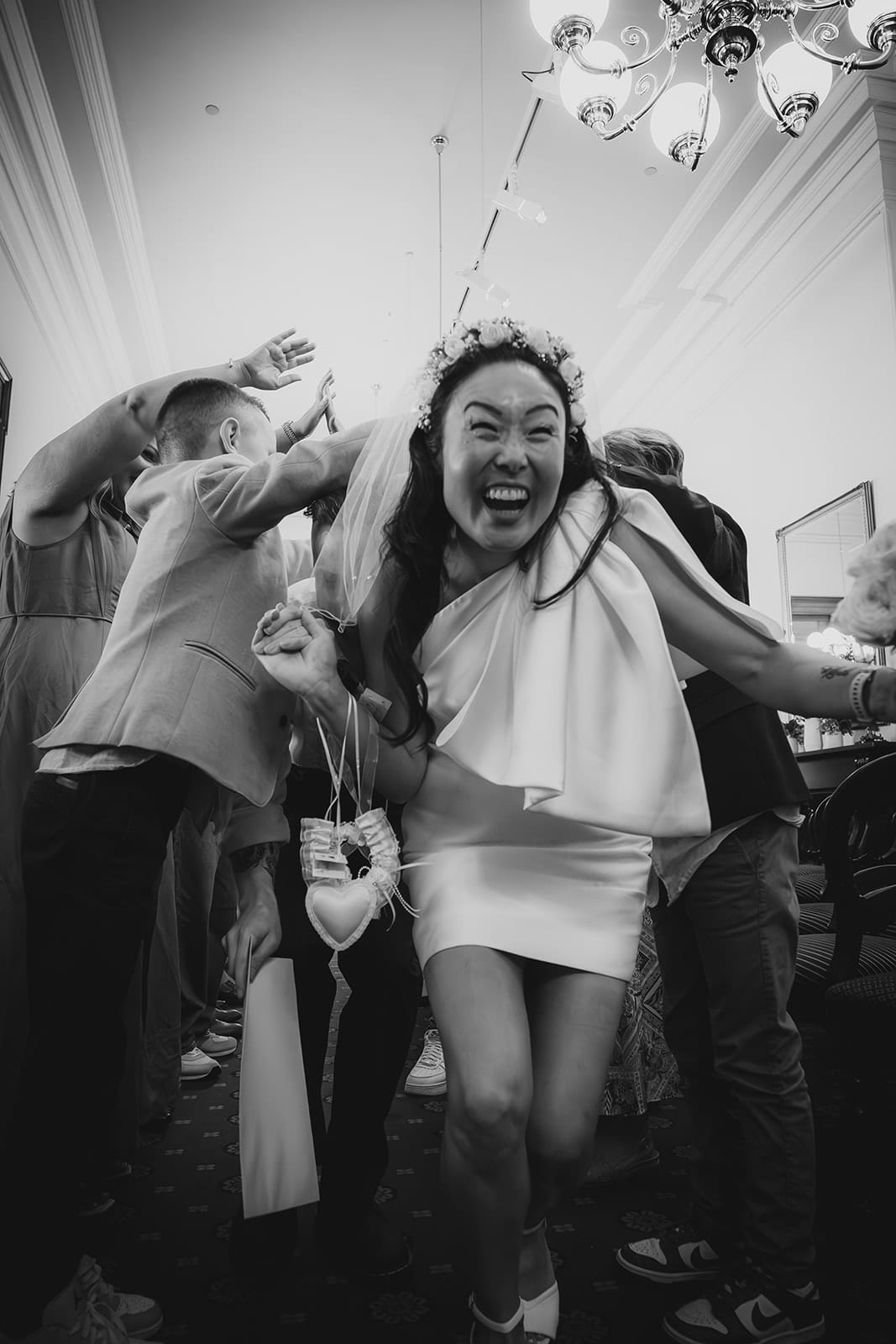 Black and white photo of Cecile laughing as she runs through a tunnel of guests’ arms