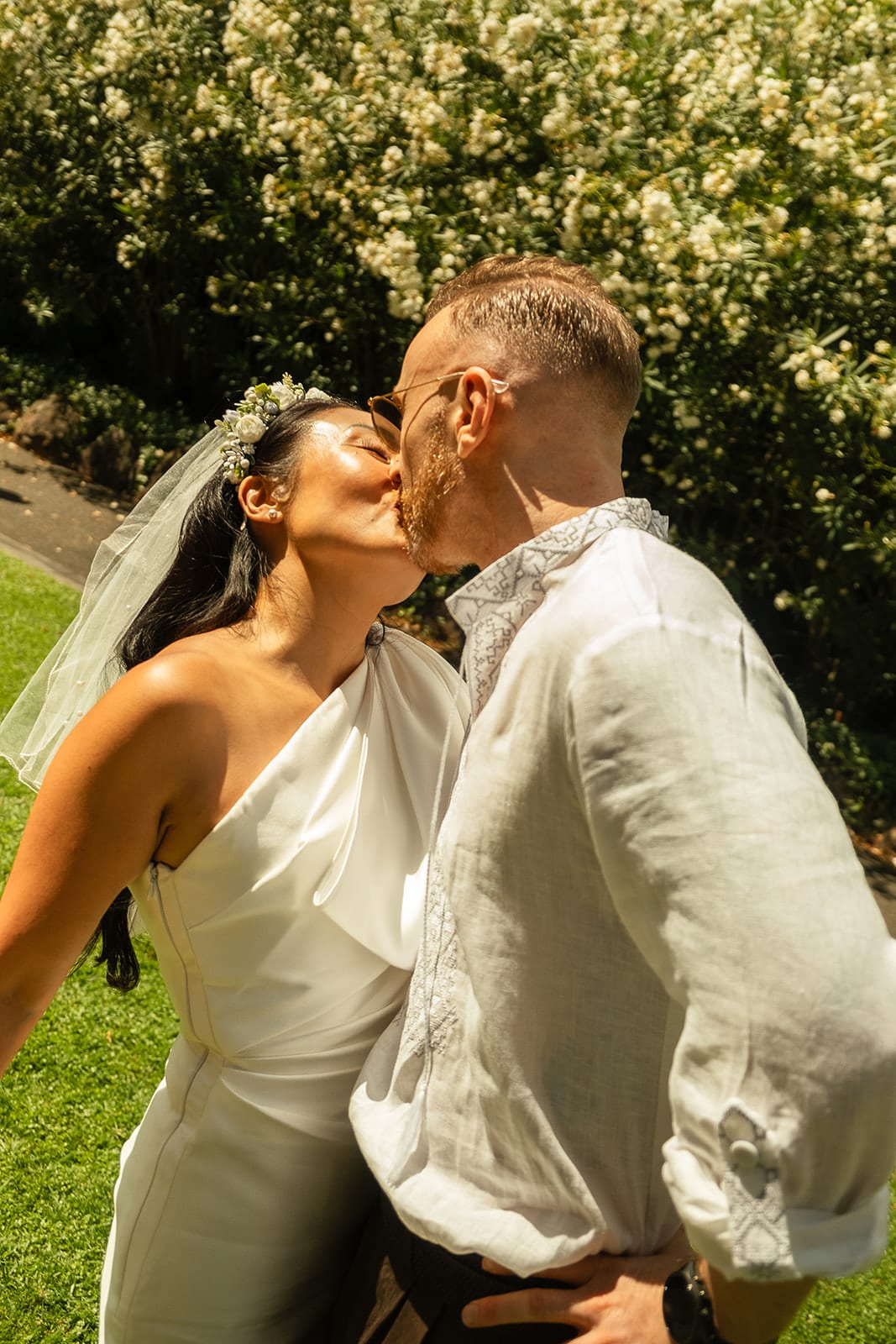 Cecile and Stefan kissing in front of the white flowers of the hedge