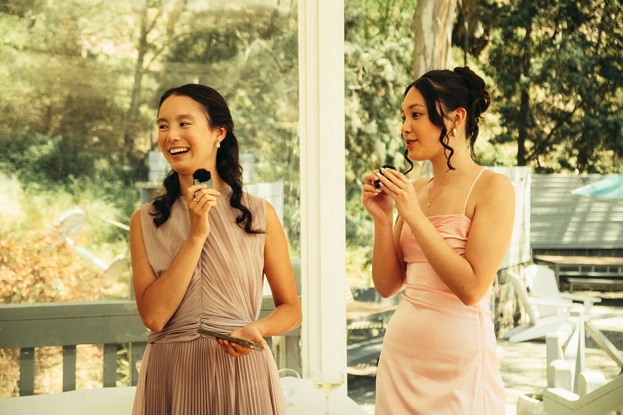 Two friends in pink dresses laughing as they give a speech with microphones on the verandah