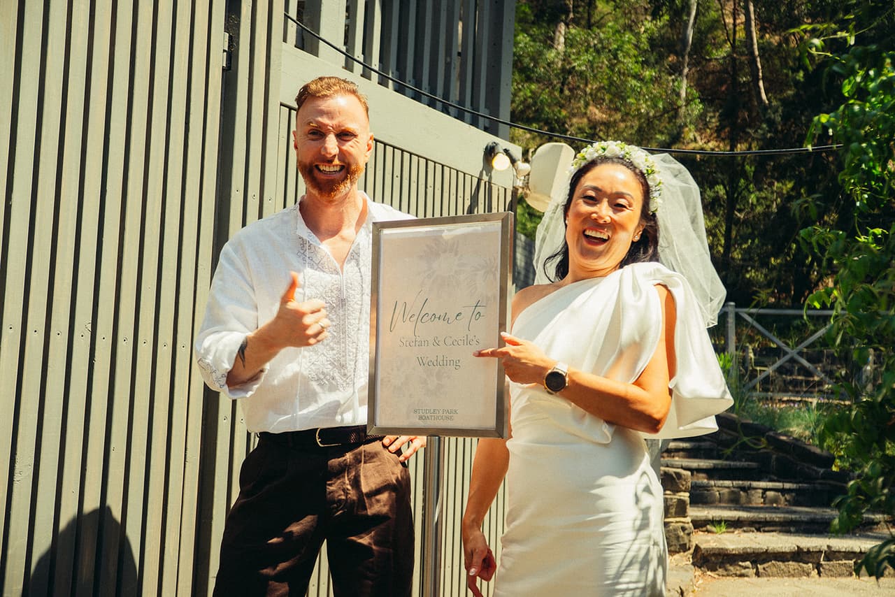 Cecile and Stefan laughing with the boathouse welcome sign that carries their first names