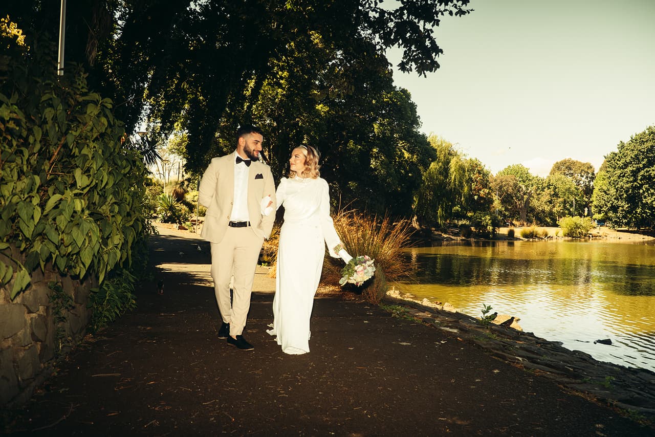 Elektra and Yasir walking along the lakeside path under overhanging trees