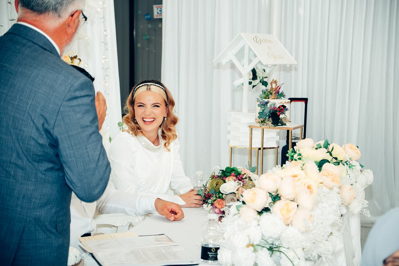 Elektra laughing at the head table as the older man in the grey suit speaks to her