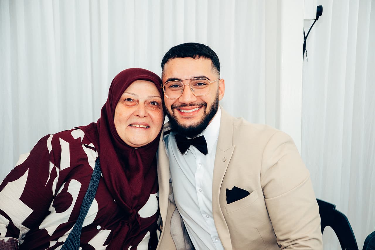 Yasir cheek to cheek with an older woman in a burgundy headscarf, both smiling