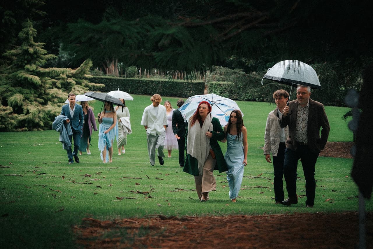Guests with clear and coloured umbrellas walking across the lawn to the ceremony