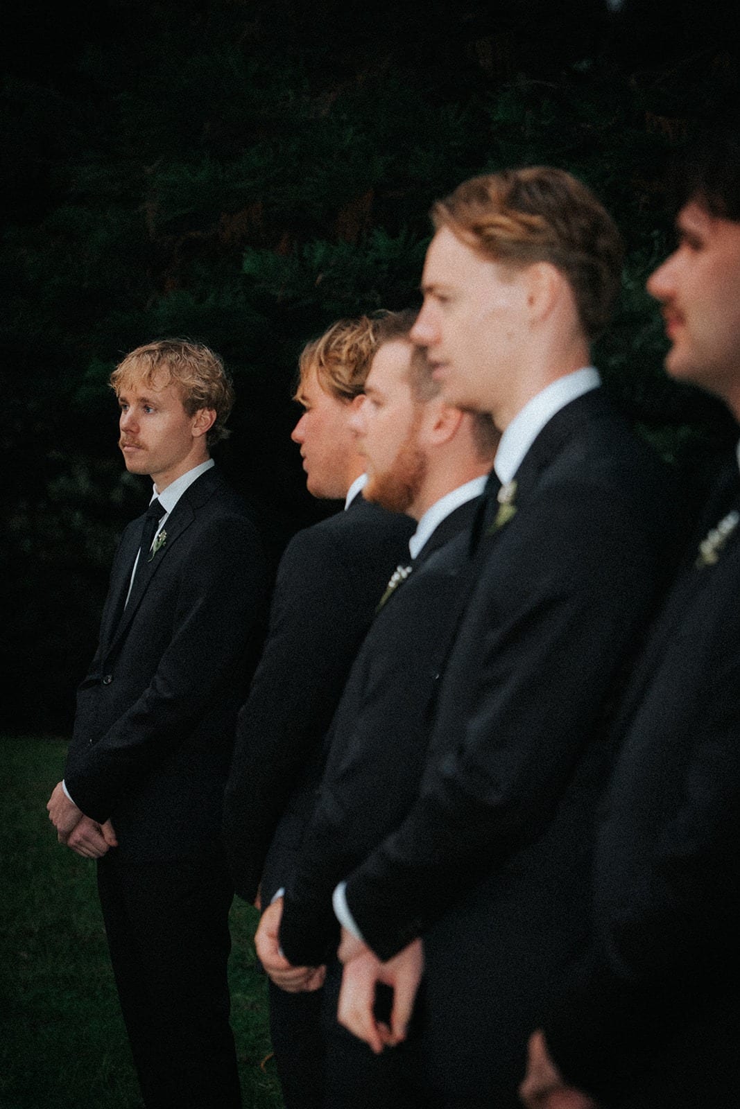Groomsmen standing in a row, hands folded, waiting for the ceremony to begin