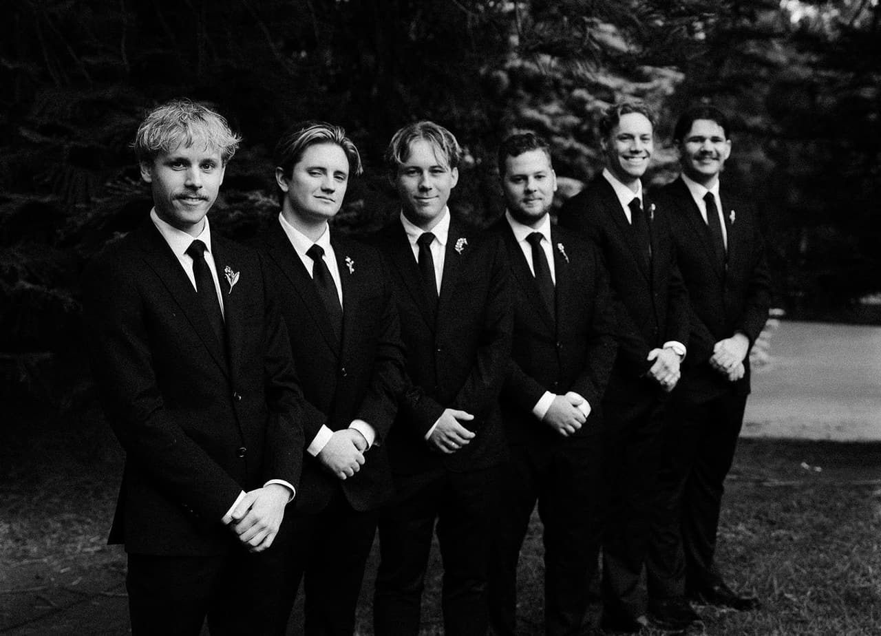 Black and white portrait of the groom and his groomsmen lined up on the lawn