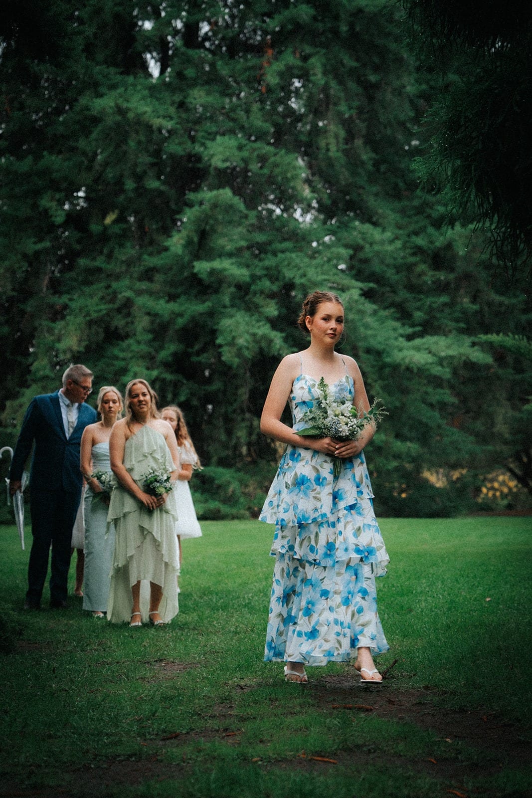 A bridesmaid in a blue floral dress walking down the grass aisle