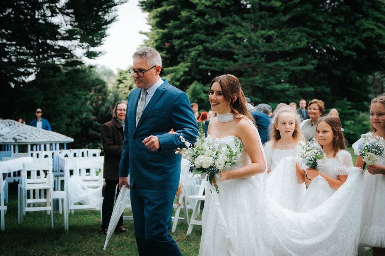 Charlotte on her father’s arm while flower girls hold her train