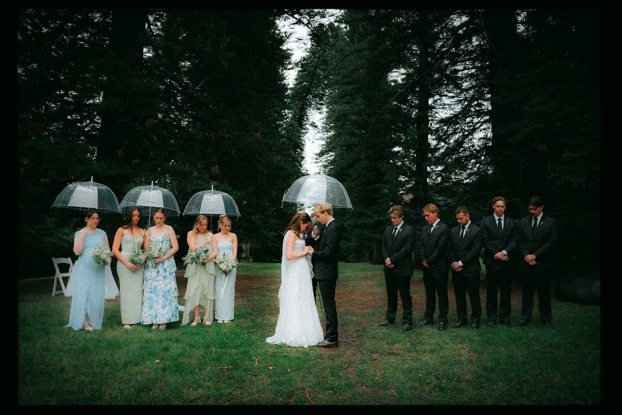 The bridal party under clear umbrellas as Eli and Charlotte stand together at the ceremony