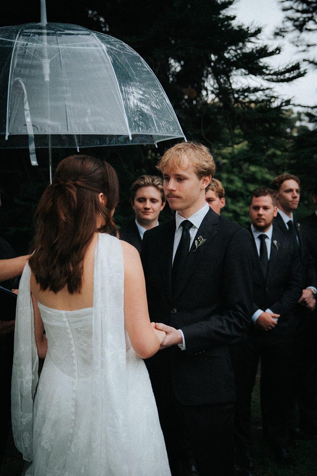 Charlotte holding Eli’s hands under a clear umbrella during the vows