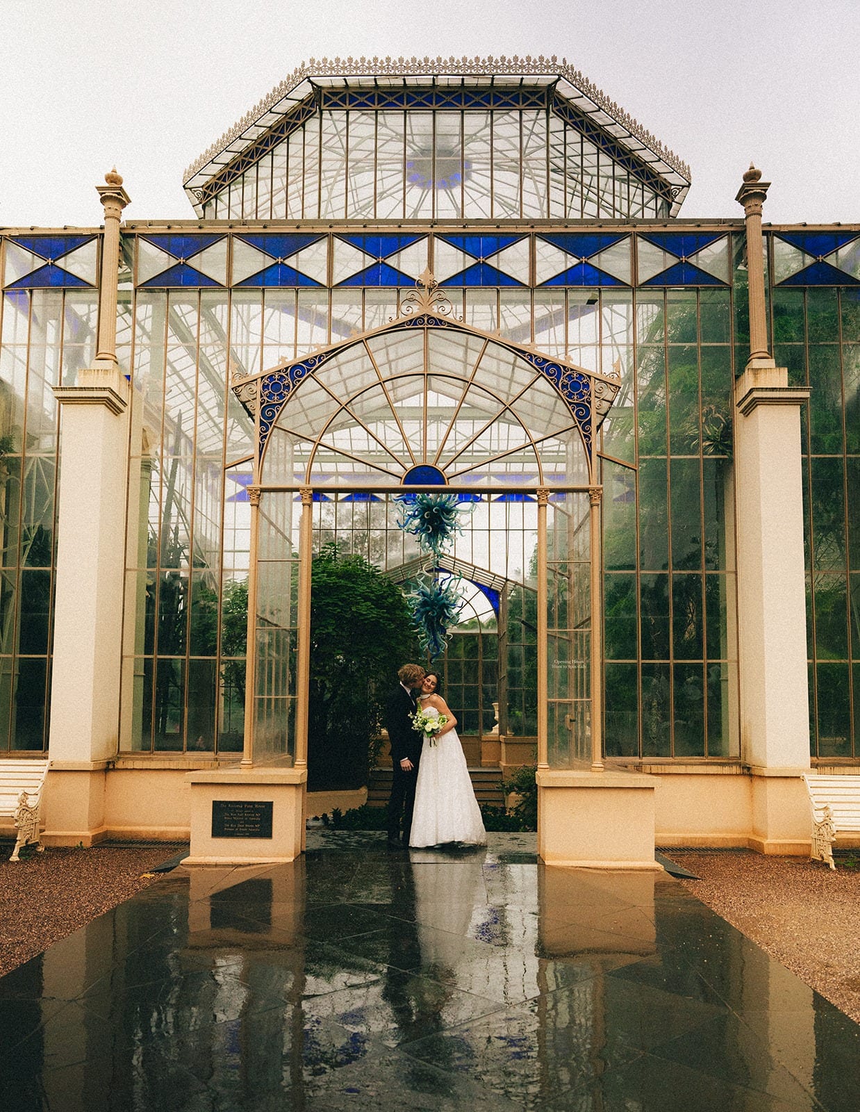Eli and Charlotte at the entrance of the Palm House glasshouse, reflected in the wet path