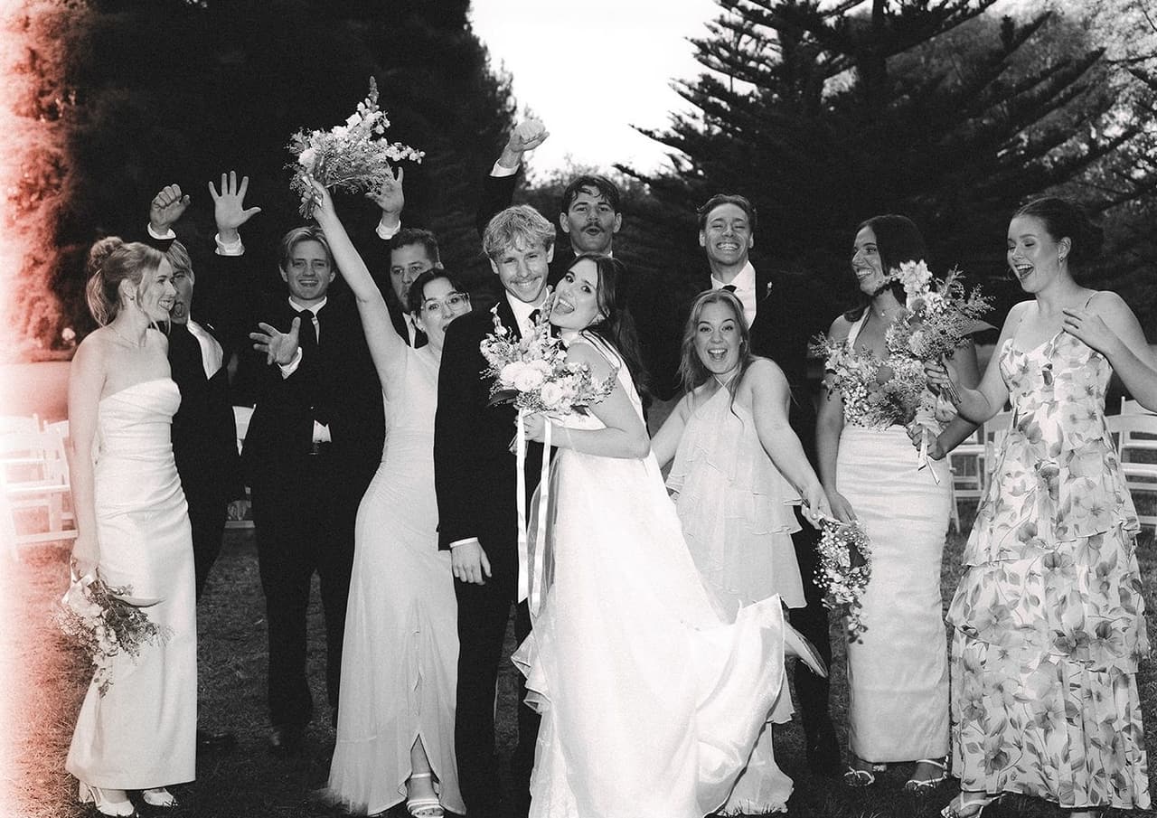 Black and white photo of the bridal party cheering with bouquets in the air