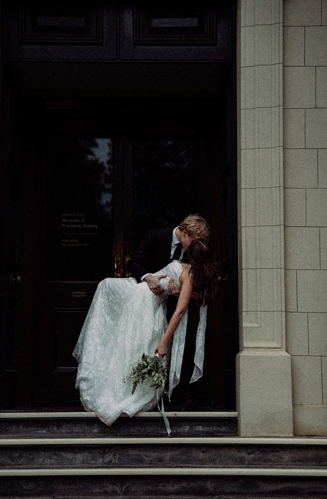 Eli dipping Charlotte for a kiss in the dark doorway of the Museum of Economic Botany