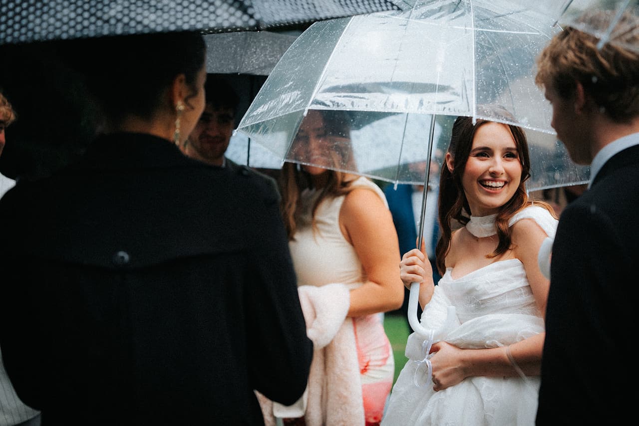 Charlotte laughing under a clear umbrella as guests gather round to congratulate her