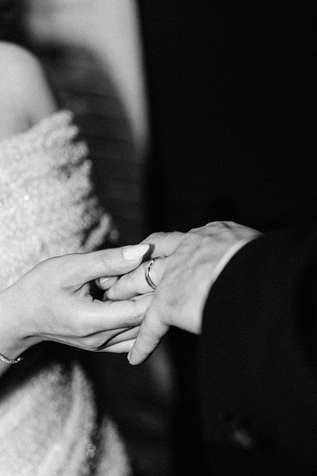 Black and white photo of Tia sliding the ring onto George’s finger