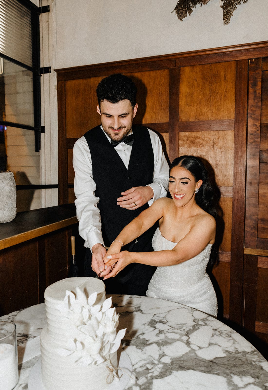 George and Tia cutting a white sculpted cake in the timber-panelled room