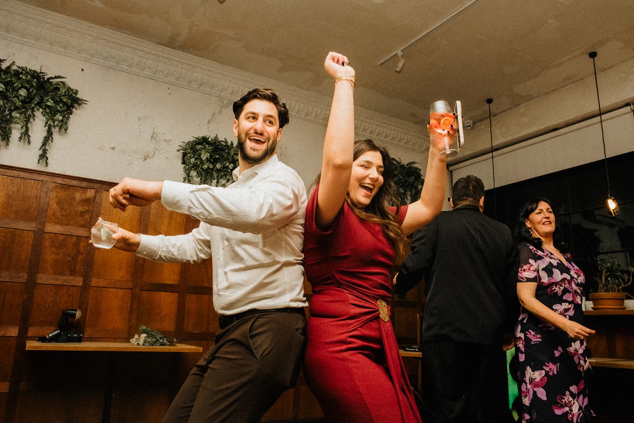 A guest in a white shirt and a woman in red dancing with their arms in the air
