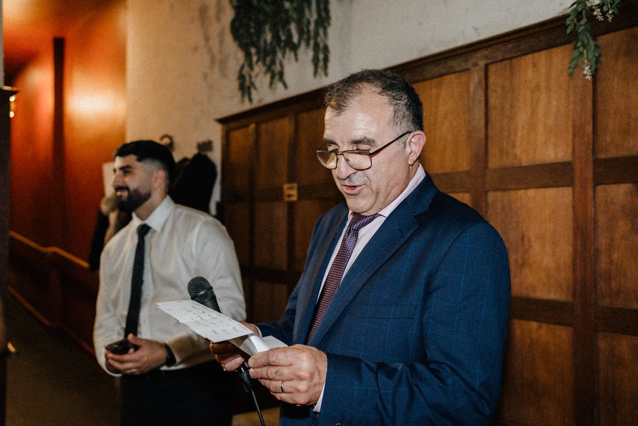 A man in a blue suit reading his speech from a page in front of the timber panelling