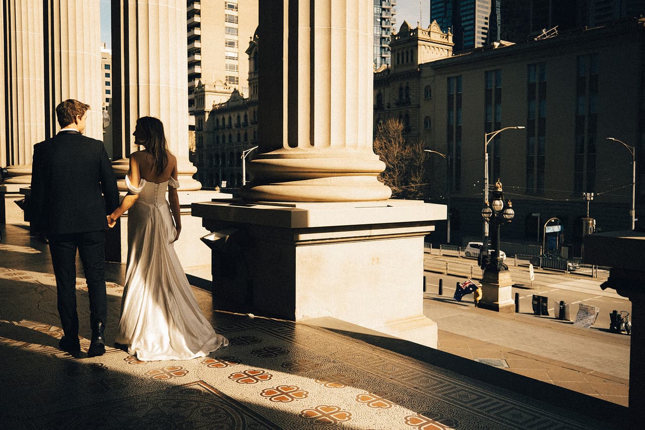 Hannah and Josh seen from behind at the edge of the Parliament House colonnade, looking out over Spring Street