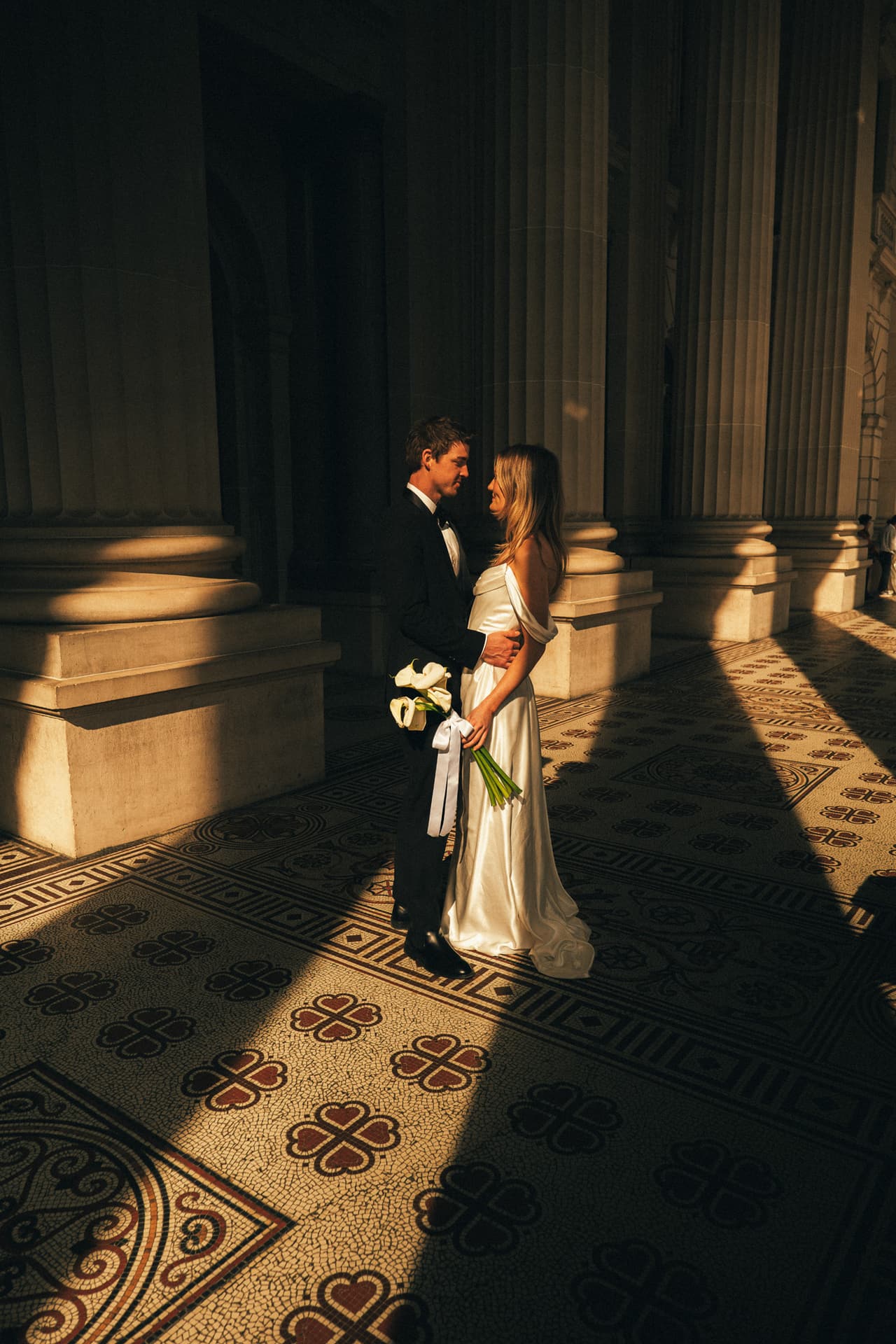 Hannah and Josh standing in a stripe of sun between the columns