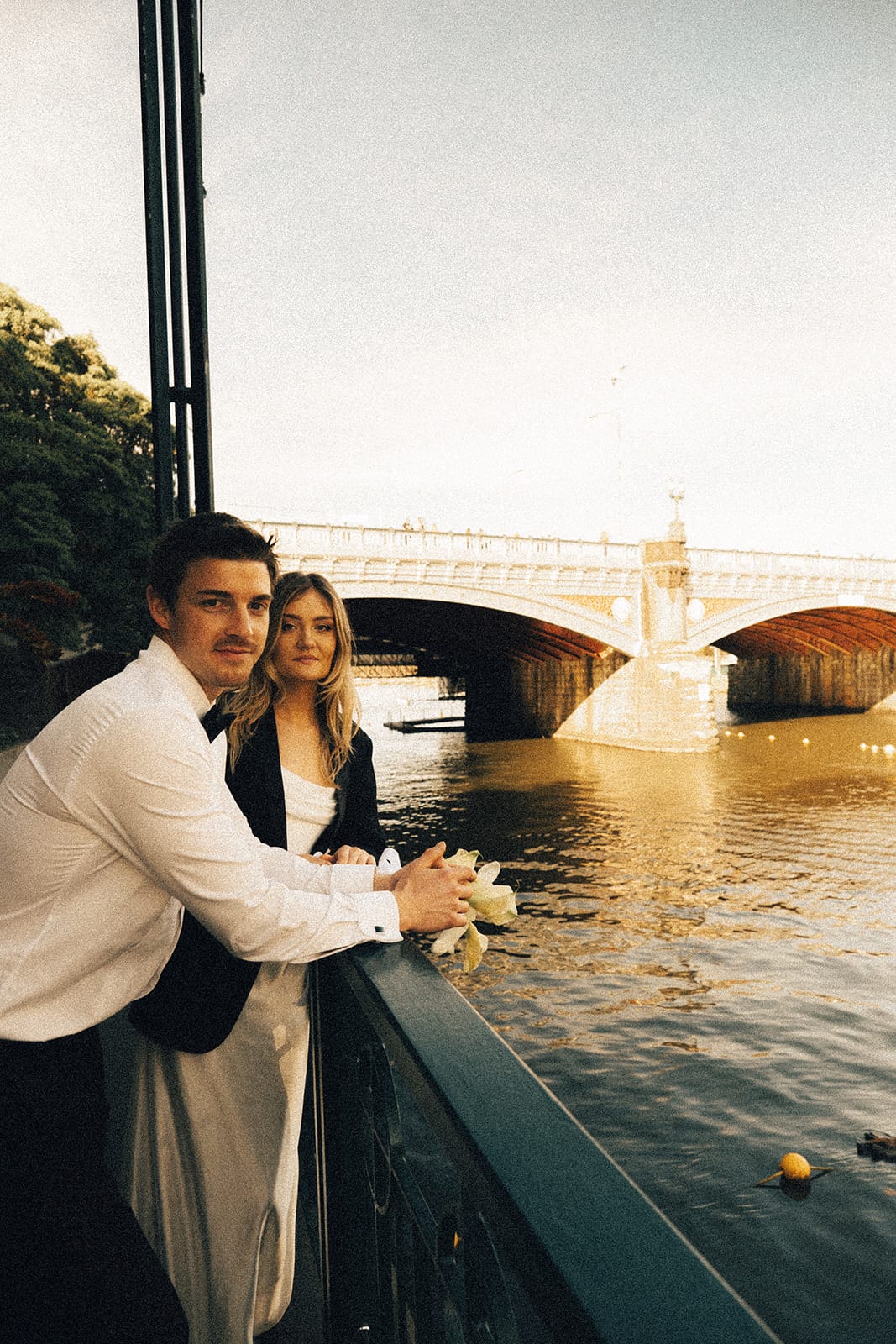 Hannah and Josh leaning on the railing over the Yarra, an arched stone bridge behind them