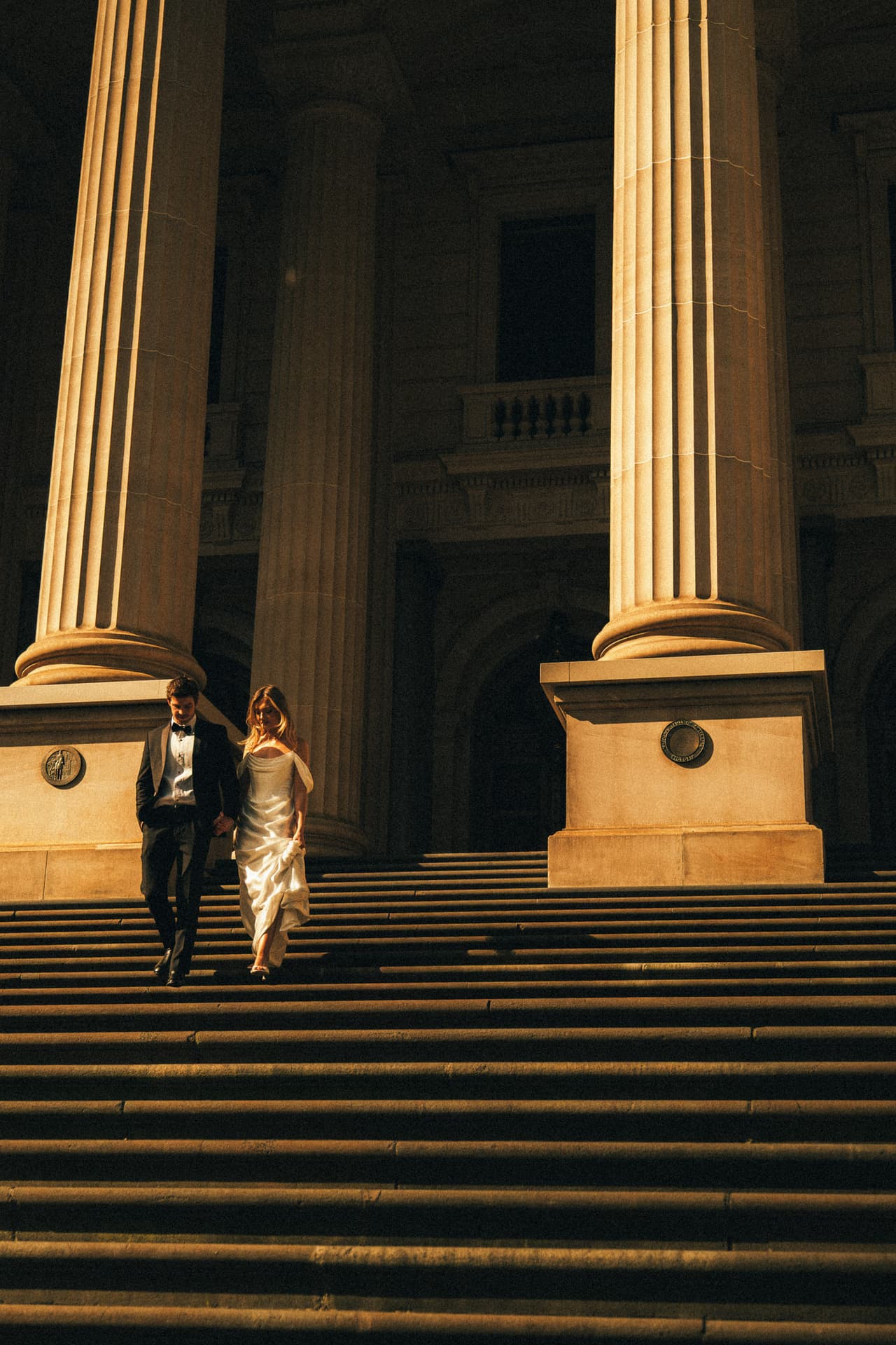 Hannah and Josh walking down the wide Parliament House steps between the columns
