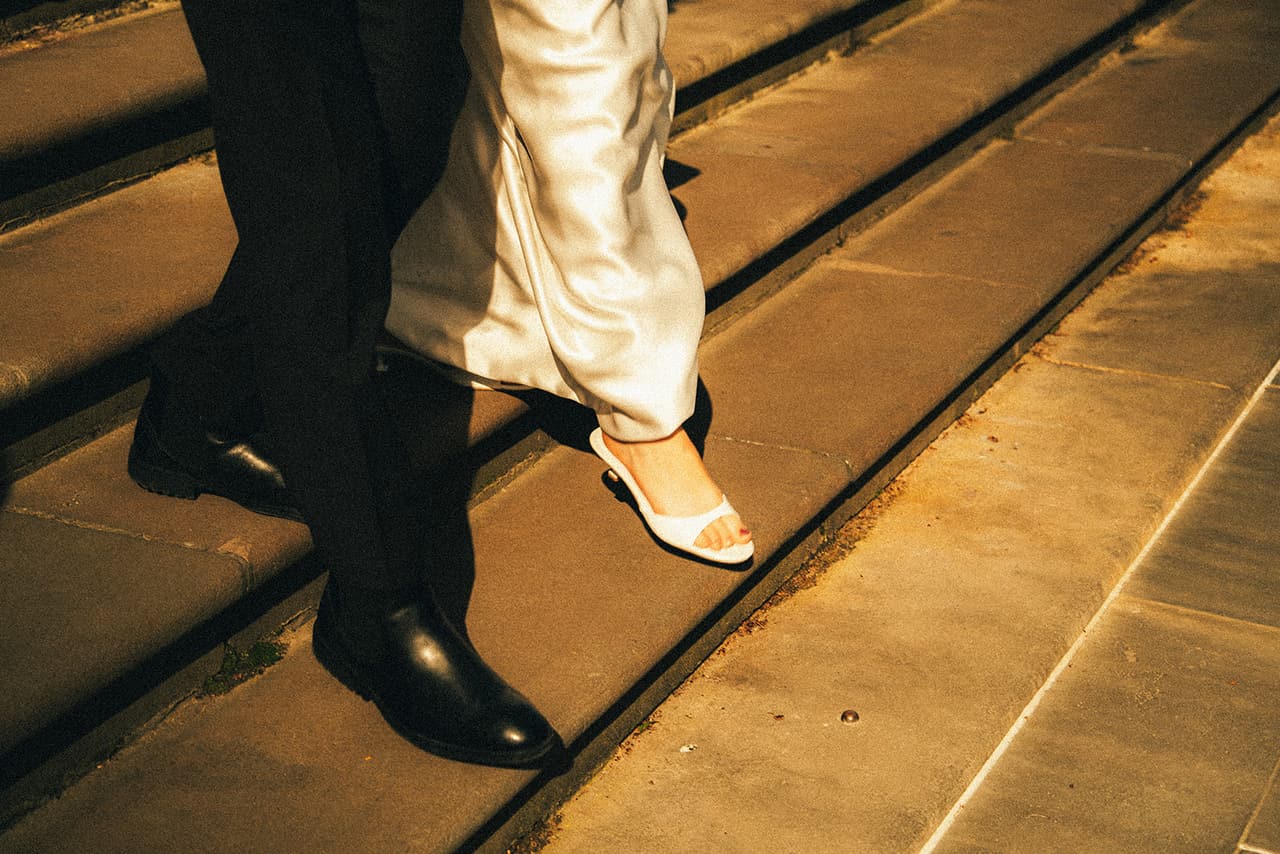 Close up of Hannah’s white heels and Josh’s polished shoes stepping down the stone steps