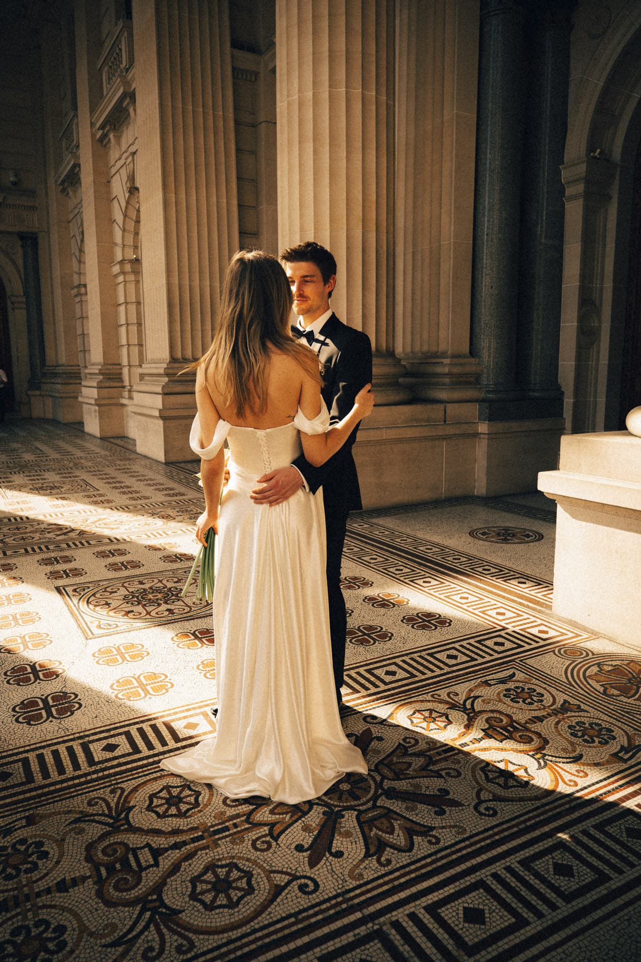 Hannah and Josh embracing on the patterned tiles of the Parliament House colonnade