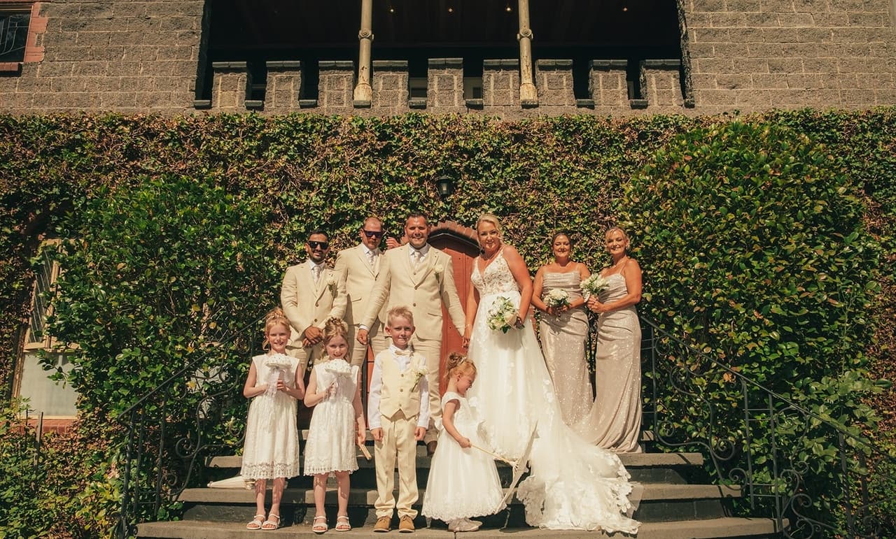 Jenna, Nick, the bridal party and the children on the castle steps in front of the ivy