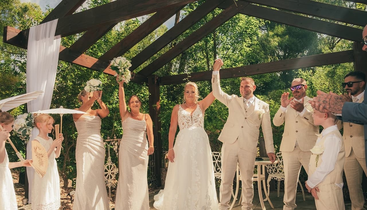 Jenna, Nick and the bridal party raising their arms under the pergola after the ceremony