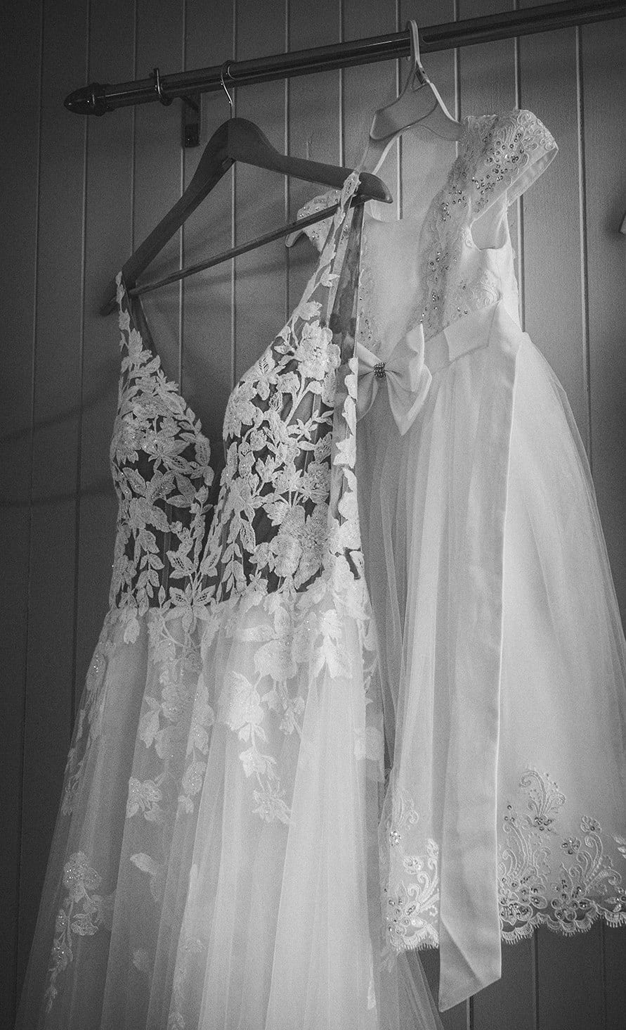 Black and white photo of Jenna’s lace wedding gown hanging on a white wall