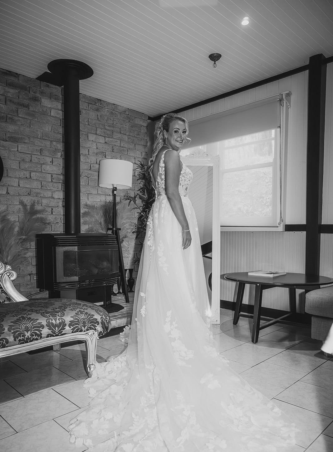Black and white photo of Jenna in her gown standing by the window of the guest room