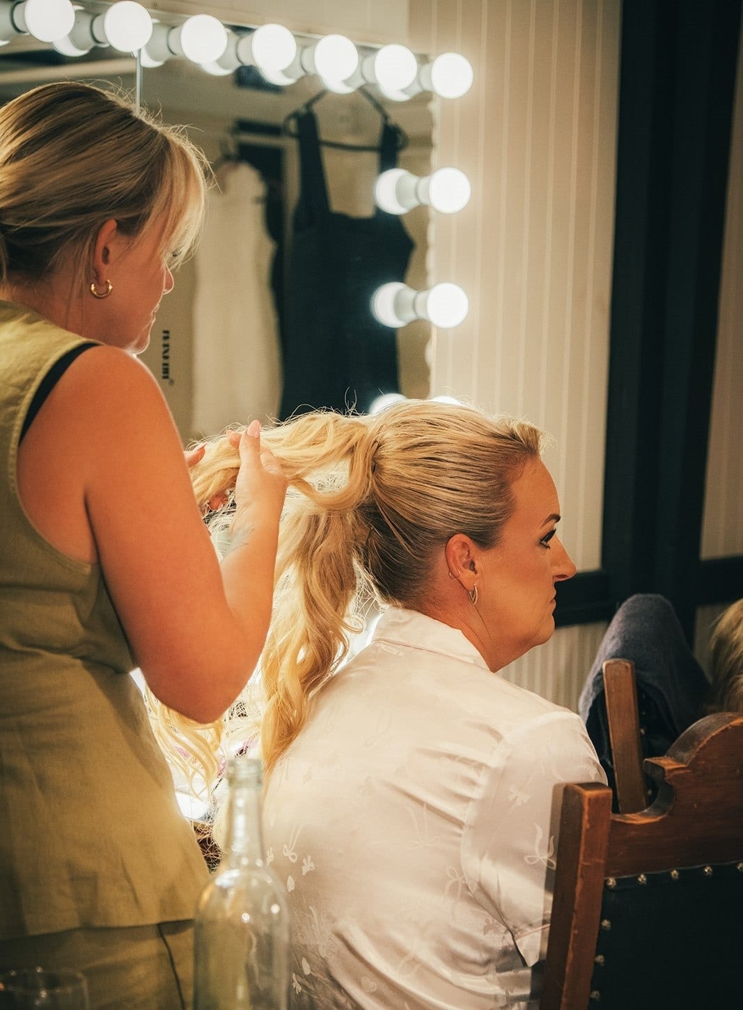 Jenna having her hair done in front of a lit mirror in the getting ready room